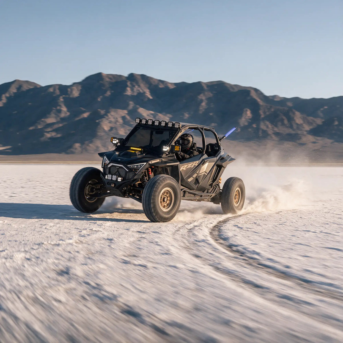 Lifestyle image of a Polaris RZR ripping through an off-road slat flats environment with mountains in the background.